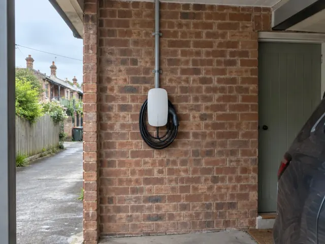 Wall-mounted EV charger on a red brick exterior wall beside a driveway in Marrickville